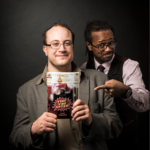 Alec Frazier and Jd Michaels. Alec is holding a copy of his book, Veni Vidi, Autism!